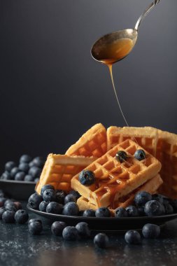 Siyah tabakta taze yaban mersini ve karamel soslu Belçika waffleları.