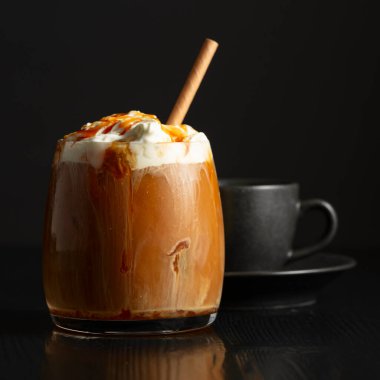 Krem şantili buzlu kahve ve karamel sosu ve siyah ahşap bir masada bir fincan sade kahve. Boşluğu kopyala.