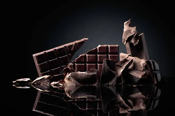 Eine Zerbrochene Schokoriegel Und Stücke Dunkler Schokolade Auf Schwarzem Reflektierendem lizenzfreie Stockfotos