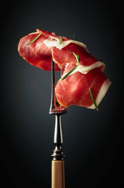 Sliced prosciutto with rosemary on a fork.