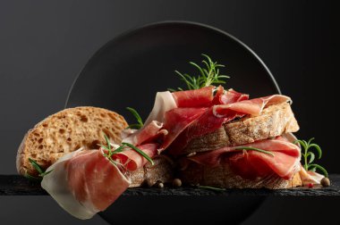 Siyah arka planda prosciutto ve biberiyeli Ciabatta. Geleneksel İtalyan atıştırması.
