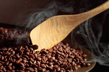 Orta pişmiş kahve çekirdekleri kızartma tavasında dumanlıdır. Boşluğu kopyala.