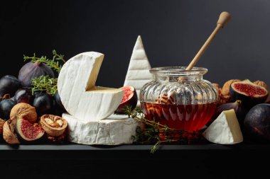 İncirli, üzümlü, cevizli, ballı ve kekikli Camembert peyniri. Siyah arka planda meyveli yumuşak peynir..