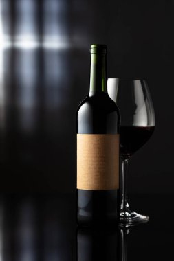 Siyah yansıtıcı arka planda cam ve bir şişe kırmızı şarap. Eski etiketli bir şişe kırmızı şarap. Metnin için alanı olan ön görünüm.
