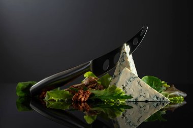 Bıçaklı mavi peynir, ceviz ve siyah arka planda taze yeşillikler. Boşluğu kopyala.