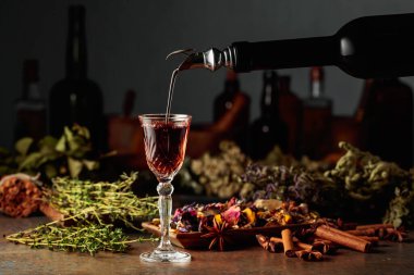 Esmer bitkisel likör ya da merhem eski bir şişeden bardağa dökülür. Kurutulmuş otlar, çiçekler, baharatlar ve eski mutfak aletleri. Bitkisel ilaç kavramı.