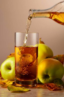 Elma şarabı şişeden bardağa dökülür. Seramik bir masada olgun elmalar ve kurumuş yapraklar..