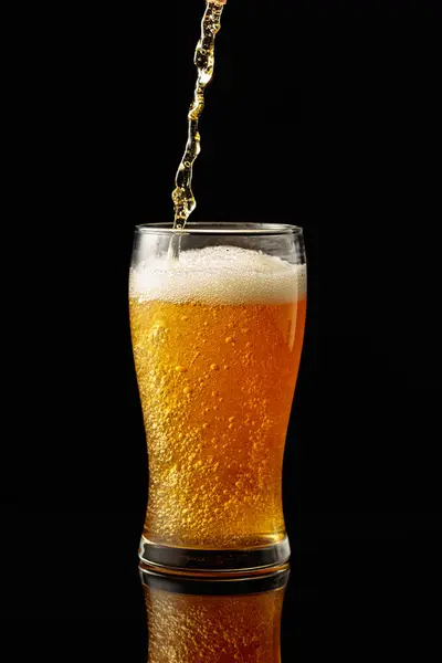 Pouring beer into a glass. Glass of beer on a black reflective background.