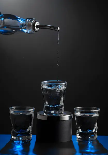 Vodka Versando Dalla Bottiglia Bicchiere Uno Sfondo Scuro Retroilluminazione Blu Immagine Stock