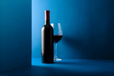 Mavi arka planda bir şişe kırmızı şarap. Boşluğu kopyala.