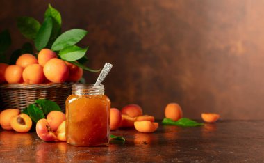 Cam kavanozda kayısı reçeli ve kahverengi bir masada taze meyve. Boşluğu kopyala.