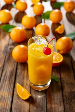 Kırmızı kirazla süslenmiş buzlu bir bardak portakal suyu. İçki ve taze meyveler eski ahşap bir masada.