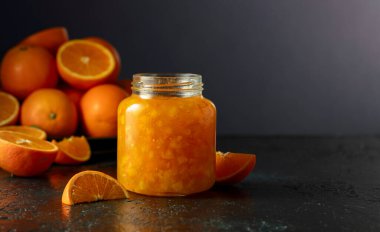 Cam kavanozda portakal reçeli ve koyu mavi bir masada taze meyve. Boşluğu kopyala.