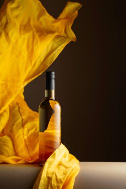 Bir şişe beyaz şarap ve koyu bir arka planda çırpınan sarı kumaş..