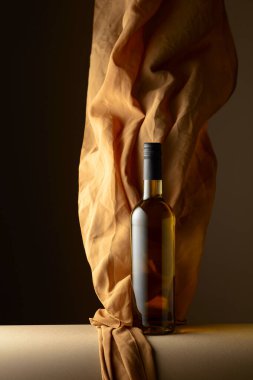Bir şişe beyaz şarap ve koyu bir arkaplanda bej rengi kumaş..