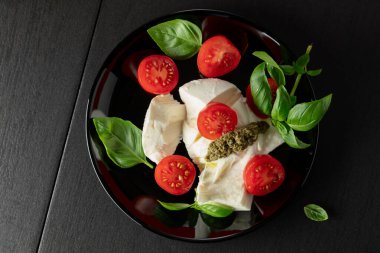 Fesleğenli Mozzarella, vişneli domates ve siyah tabakta pesto sosu. Geleneksel İtalyan mutfağı. Üst görünüm.