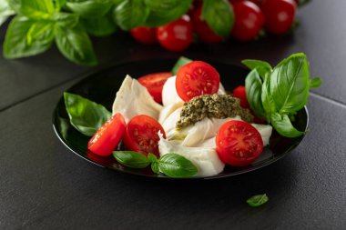 Fesleğenli Mozzarella, vişneli domates ve siyah tabakta pesto sosu. Geleneksel İtalyan mutfağı.