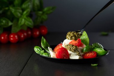 Fesleğenli Mozzarella, vişneli domates ve siyah tabakta pesto sosu. Geleneksel İtalyan mutfağı.