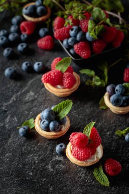 Siyah arka planda naneli taze ahududu ve yaban mersinli küçük tartlar..