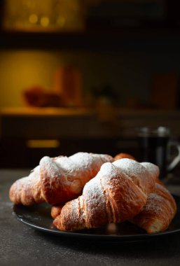 Taze kruvasan ve mutfak masasında sade kahve. Şeker tozu serpiştirilmiş kruvasanlar. Seçici odak.