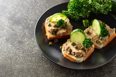 Pate, taze salatalık, kapari ve maydanozlu sandviç. Siyah tabakta ezmeli tost..