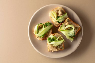 Pate, taze salatalık, kapari ve maydanozlu sandviç. Bej arka planda ezmeli tost. Üst görünüm, alanı kopyala.