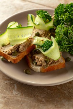 Bej tabakta ezmeli tost. Pate, taze salatalık, kapari ve maydanozlu sandviç..