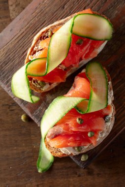 Tütsülenmiş alabalık, krem peynir, taze salatalık ve eski bir kesim tahtasında kapari..