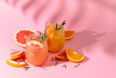 Greyfurt, portakal, biberiye ve buzlu yaz kokteylleri. İçkiler pembe arka planda, palmiye yaprağı gölgesinde. Yaz, tropikal, taze kokteyl konsepti.