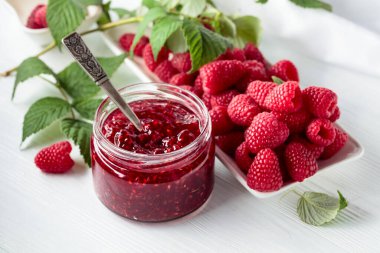 Ahududu reçeli kavanozu ve beyaz ahşap masa yapraklı taze böğürtlen..