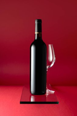 Bottle of red wine and an empty wine glass on a red background.