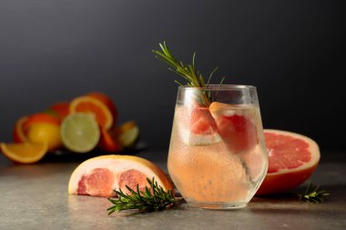 Buzlu, biberiyeli ve greyfurtlu kokteyl cin toniği. Arka planda kokteyl yapmak için çeşitli turunçgil meyveleri var..