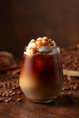 Krem şanti ve karamel soslu buzlu karamel latte. Kahverengi bir masada serinletici ve tatlı bir kahve..