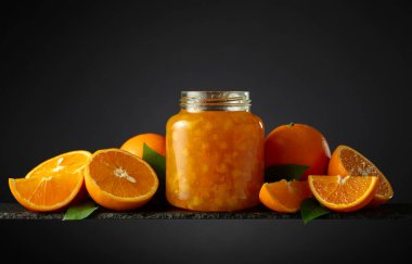 Cam kavanozda portakal reçeli ve taze meyve. Siyah arka planda güzel bir kesişme. Boşluğu kopyala.