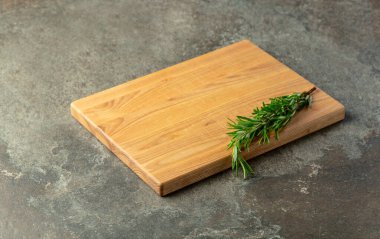 Taş bir masanın üzerinde kesme tahtası ve biberiye. Mutfak geçmişi. Boş tahta kesme tahtası, ürün görüntüleme alanı.