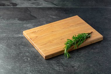 Siyah taş bir masa üzerinde kesme tahtası ve biberiye. Mutfak geçmişi. Boş tahta kesme tahtası, ürün görüntüleme alanı.