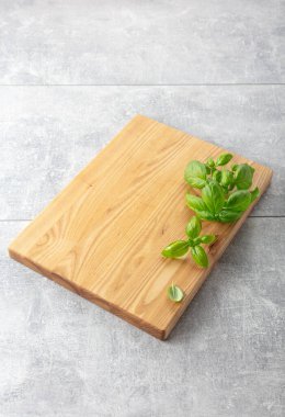 Gri bir mutfak masasında fesleğen ve tahta kesmek. Mutfak geçmişi. Boş tahta kesme tahtası, ürün görüntüleme alanı.