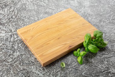 Gri bir mutfak masasında fesleğen ve tahta kesmek. Mutfak geçmişi. Boş tahta kesme tahtası, ürün görüntüleme alanı.