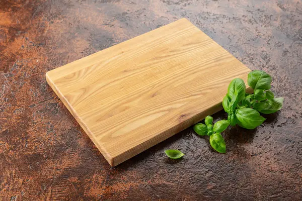 Kahverengi mutfak masasında fesleğen ve tahta kesme. Mutfak geçmişi. Boş tahta kesme tahtası, ürün görüntüleme alanı.