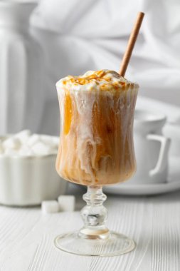 Krem şantili ve karamel soslu buzlu karamel latte, beyaz bir masada ferahlatıcı ve tatlı bir kahve..