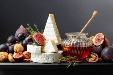 İncirli, üzümlü, cevizli, ballı ve kekikli Camembert peyniri. Siyah arka planda meyveli yumuşak peynir..