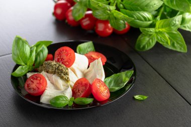 Fesleğenli Mozzarella, vişneli domates ve siyah tabakta pesto sosu. Geleneksel İtalyan mutfağı.