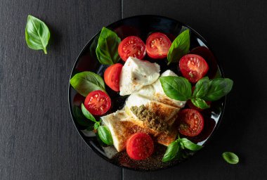 Fesleğenli Mozzarella, vişneli domates ve üzerine Akdeniz baharatları serpiştirilmiş pesto sosu. Geleneksel İtalyan mutfağı. Üst görünüm.