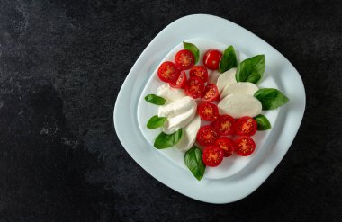 Siyah taşlı arka planda fesleğen ve kiraz domatesli Mozzarella. Kopyalama alanı olan üst görünüm.