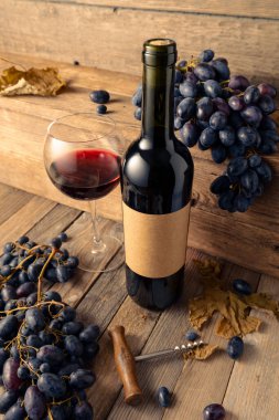 Eski ahşap bir masada bir şişe kırmızı şarap ve mavi üzüm. Eski boş bir şişede. Boşluğu kopyala.