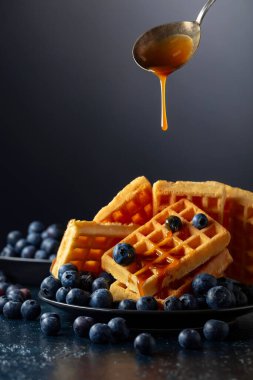 Siyah tabakta taze yaban mersini ve karamel soslu Belçika waffleları.