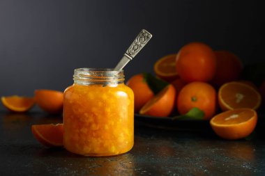 Cam kavanozda portakal reçeli ve koyu mavi bir masada taze meyve..