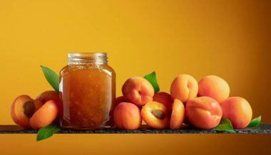 Cam kavanozda kayısı reçeli ve taze meyve. Turuncu arka planda tatlı bir kesişme. Boşluğu kopyala.