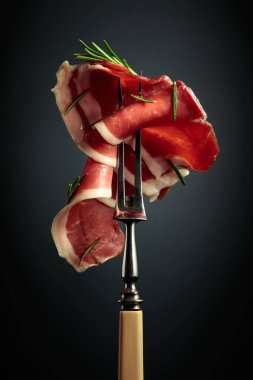 Sliced prosciutto with rosemary on a fork.