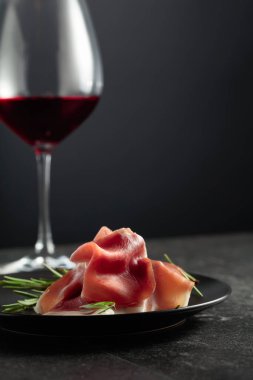 Prosciutto biberiye ve siyah bir zemin üzerine kırmızı şarap ile. Metniniz için kopya alanı.